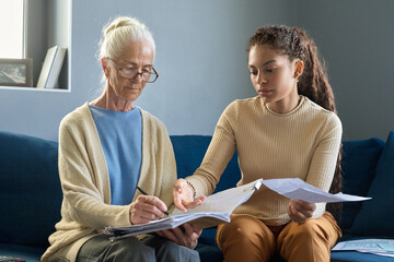 Teenage girl pointing at payment bill while explaining financial information to grandmother sitting...