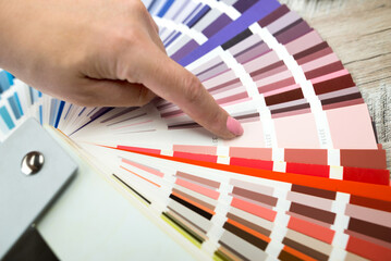 Person with a finger shows to the selected color in the palette for paint tinting. Colored catalog...