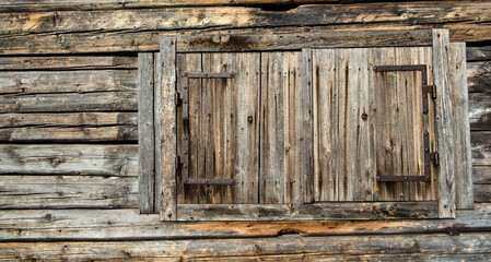Background and wood texture from a wall of an old wooden house with windows closed by shutters