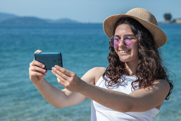 Fototapeta premium relaxed young woman taking a selfie or direct video with phone on the beach