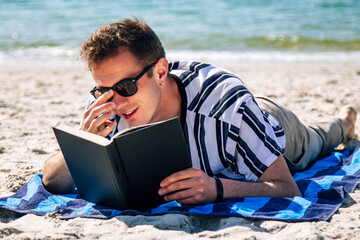 relaxed young man reading a book on the beach