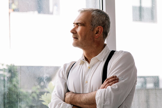 Casual Middle Aged Man With Crossed Arms At Home Or Office Looking Out The Window