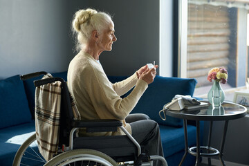 Side view of retired woman with disability going to take pill from small plastic pill-box while...