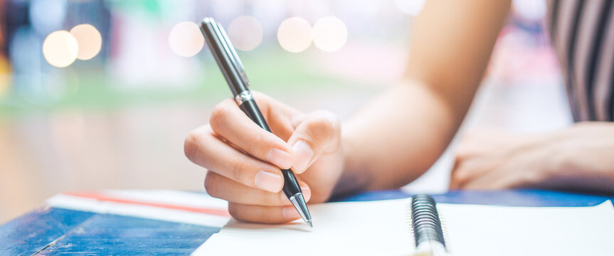Woman hand is writing on a notepad with a pen on wooden desk.