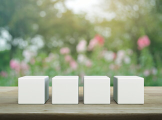 Four white block cubes on wooden table over blur pink flower and tree in garden