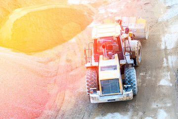 A large single-bucket tractor loader in close-up loads gravel and sand