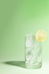 Cold glass full of ice with a lime, ready to serve light green with cast shadow.
