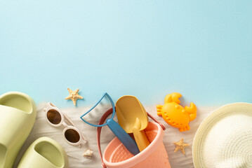 Blissful summer vacation with children by the seaside. Above view snapshot of sand with sand toys for kids, panama, slippers, sunglasses and starfish on isolated blue background with copyspace