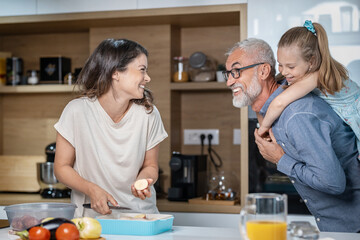 Young woman laughing at her father as he plays with his granddaughter in the kitchen