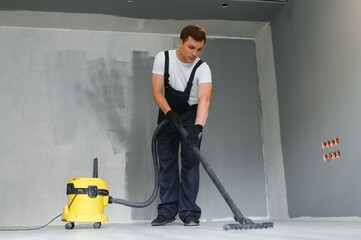 male worker in overall vacuum cleaning during apartment renovation