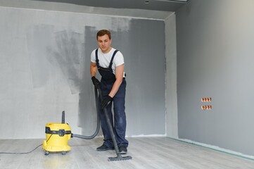 male worker in overall vacuum cleaning during apartment renovation