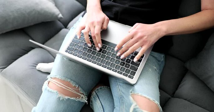 Woman in jeans sitting on sofa at home and typing on laptop keyboard closeup 4k movie slow motion. Freelance and remote work online concept 