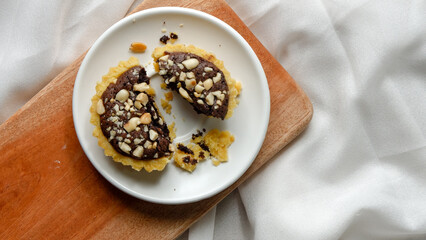 brownie cake in pie are sprinkled with chopped nuts on top of the white saucer on wooden board.