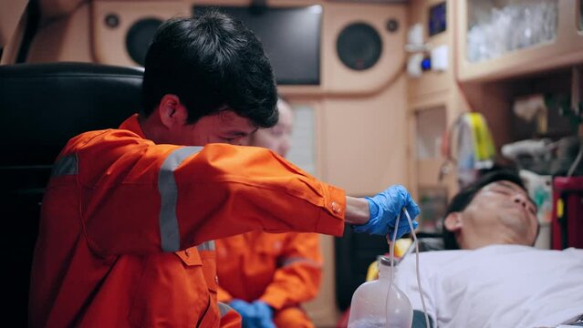 Asian emergency medical technician (EMT) or paramedic inserting an saline line into a patient in ambulance car