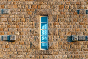 Fototapeta na wymiar Old window on the wall. A window on the stone wall of a tower. Through it, you can see the mesh spiral staircase.