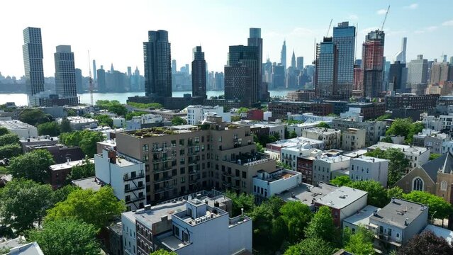 Aerial flyover neighborhood in Brooklyn with river and skyline in Manhattan in background - panorama wide shot