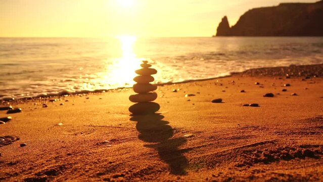 Pyramid stones on the seashore with warm sunset on the sea ocean background. Happy holidays. Sandy beach, calm sea, travel destination. Concept of happy vacation on the sea, meditation, spa, calmness.