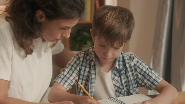 Young mother explaining homework with math exercises her son at table indoors