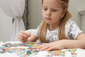 Fototapeta premium Little child picks up picture from pieces of puzzles