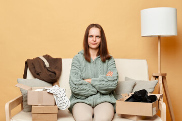 Sad confused offended woman shopaholic customer sitting on sofa unpack parcel delivery box against...