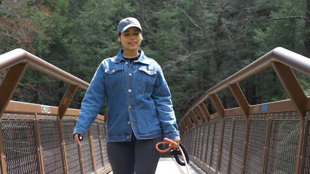 Young Happy Woman Walks Her Dog Across Metal Bridge In Upstate New York Hiking Trail Park. She Looks Full Of Joy Walking With Her Companion With Green Forest Background. Brown Senior Medium Canine 4K