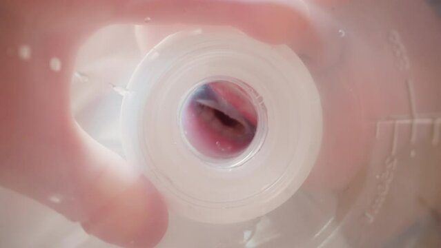 Thirsty little child holds bottle with fingers and squeezes and spreads rubber nipple with lips. Toddler puts down empty bottle macro low angle shot