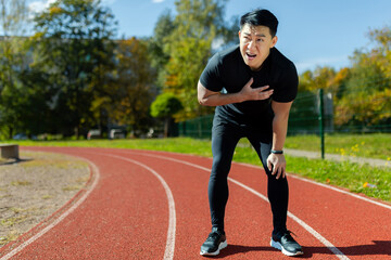 Heart attack while running and doing fitness and active exercise in stadium, asian mature man has...