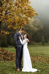 tall bride and groom hugging against the backdrop of autumn nature. walk of a cute couple in nature. newlyweds after the ceremony. wedding day in autumn