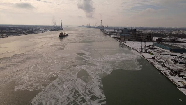 Cargo vessel transports goods on icy river of Detroit with cityscape in both sides