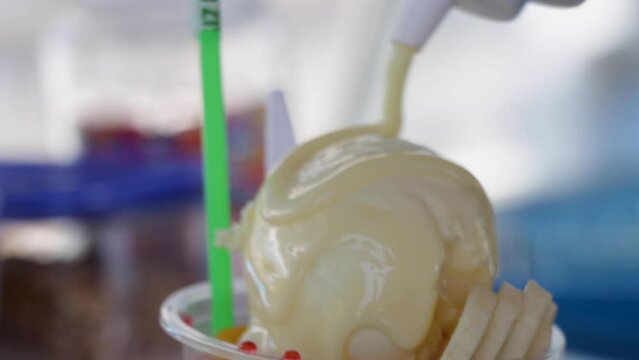 Snow cone with condensed milk being dropped in slow motion over an ice cream ball, topped with banana and fruit-flavored syrups, beach dessert, Costa Rica
