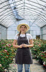 Portrait of female gardener in apron working with roses growing them in the greenhouse.