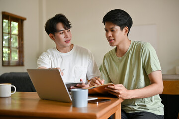 A smart young Asian male college student is tutoring and helping his friend with math at home.