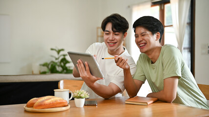 Two cheerful Asian men are watching funny videos on the internet through a tablet