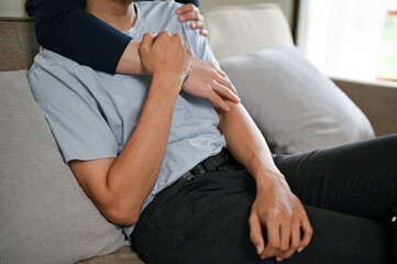 Cropped image of a happy gay couple hugging each other on a couch in the living room.