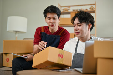 A happy Asian man checking and preparing shipping orders and working with his boyfriend