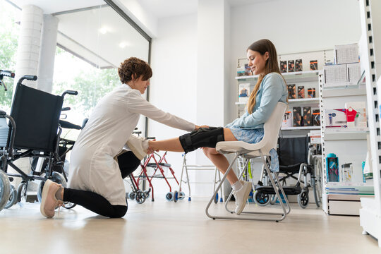 Orthopedist woman putting a knee brace on a young client