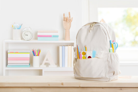 School backpack with different colorful stationery on table in room