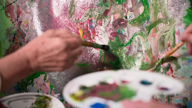 talented pensioners apply strokes with brush and paint on a modern painting on canvas, close-up hand