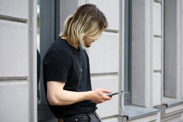 Guy with long hair standing on a street with smartphone in hands. Using phone outdoor, mobile communication