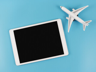 flat lay of digital tablet with blank black  screen and airplane model  isolated on blue background. travel planning concept.