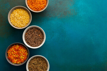 Multicolored lentils in bowls on an emerald green background, yellow and brown, green and orange...