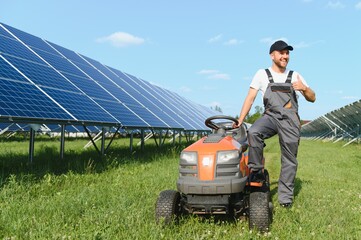 Fototapeta premium A man mows the grass near the solar panels. Green energy