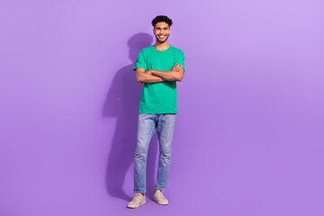 Fototapeta na wymiar Full length body photo of young confident man wear green t-shirt denim levis brand jeans folded arms smiling isolated on purple background