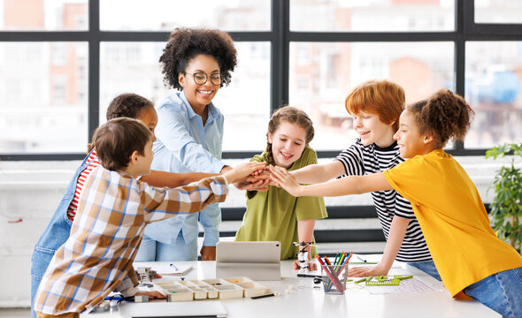Teacher and joyful students celebrate   successful completion of collective school work in a bright classroom