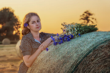 Portrait of a young girl near a haystack with a bouquet of wildflowers, a beautiful woman in the rays of the setting sun. Woman in retro pink dress in field.