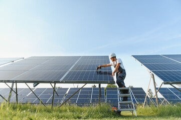 Side view of male worker installing solar modules and support structures of photovoltaic solar...
