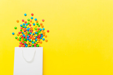 shopping paper gift bag in corner full of assorted traditional candies falling out on colored background with copy space. Happy Holidays sale concept
