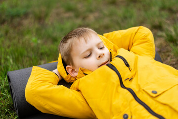 A young boy in a jacket lies in a green forest in autumn, spring. Rest, relaxation in nature.