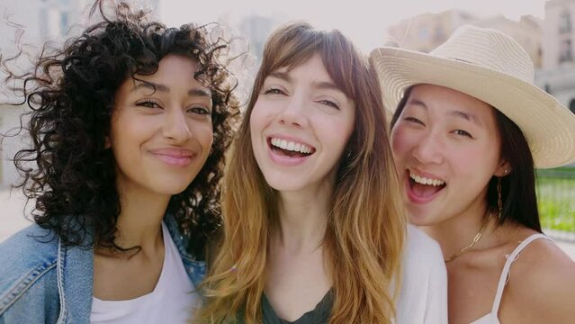 Portrait of three smiling young diverse women having fun together on city street. Happy female friends enjoying day off at weekend over urban background. Friendship and youth community concept.