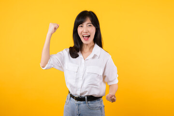 Portrait beautiful young asian woman happy smile with fist up victory gesture expression cheerful her success achievement against yellow studio background. Woman day winner celebration concept.